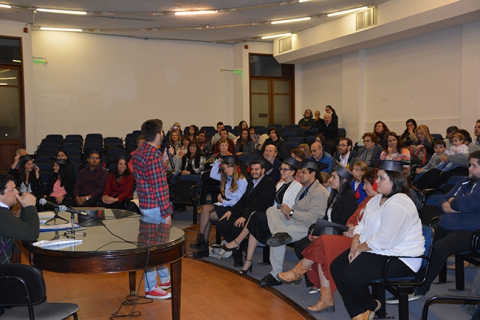 Fotografía durante la actividad. Se aprecia el auditorio con egresados/as y sus familiares y el Docente Bruno Cancio de espaldas tomando la palabra.