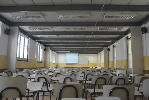 Fotografía desde el fondo del salón 1 en la que se ven silla, los parlantes colocados, y el pizarrón al fondo